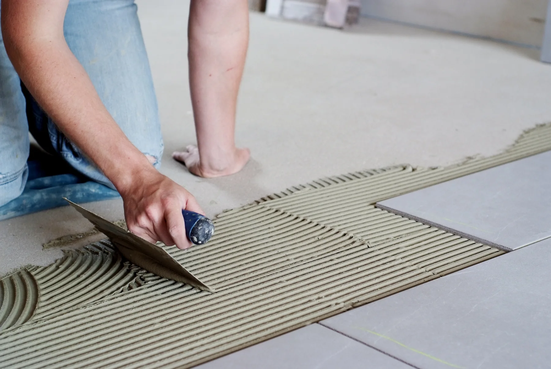 Handwerker trägt Fliesenkleber mit einer Zahnkelle auf den Boden auf