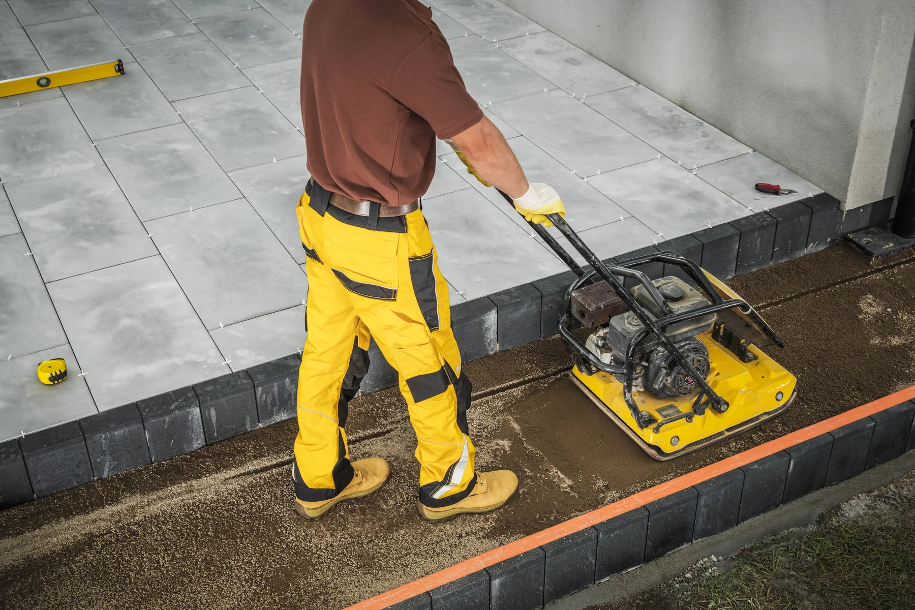 Terrassenbau – Unterbau verdichten Handwerker verdichtet den Unterbau einer Terrasse mit einer Rüttelplatte