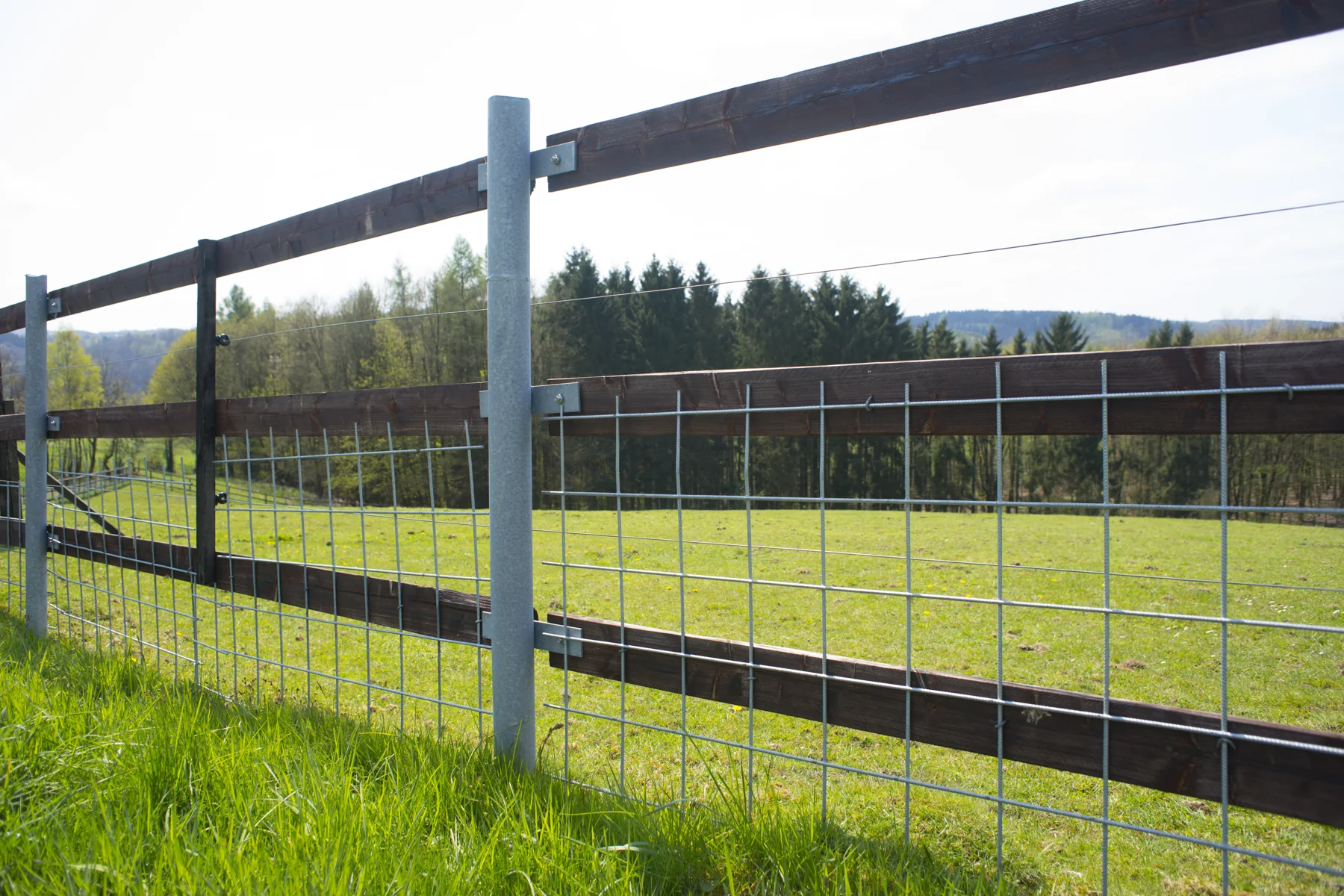 Offener Gitterzaun aus Metall und Holz an einer Wiese